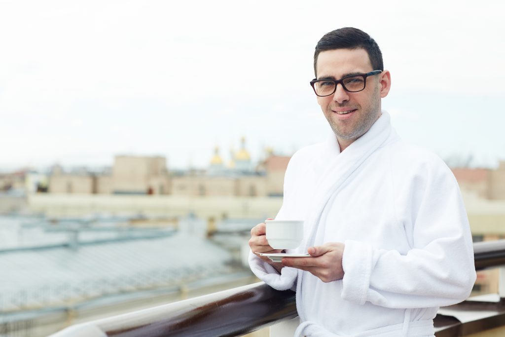 Young man in white bathrobe having tea on balcony in the morning