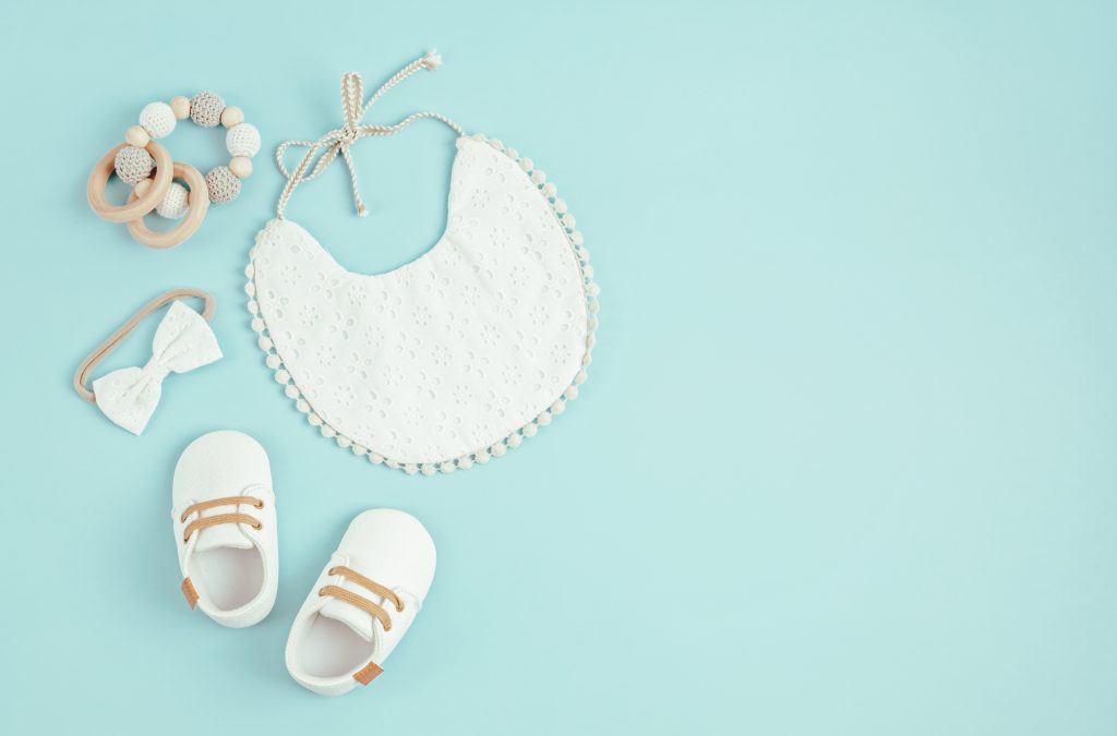 Baby shoes, bib and teether on blue background. 